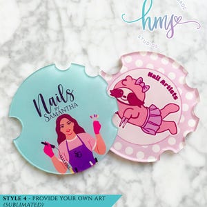 May include: Two round coasters with a scalloped edge. The left coaster is light blue with the text "Nails by Samantha" in black and a woman with pink gloves holding a nail drill. The right coaster is pink with white polka dots and a pink sloth wearing a pink tutu and a pink bow. The text "Nail Artists" is in black.