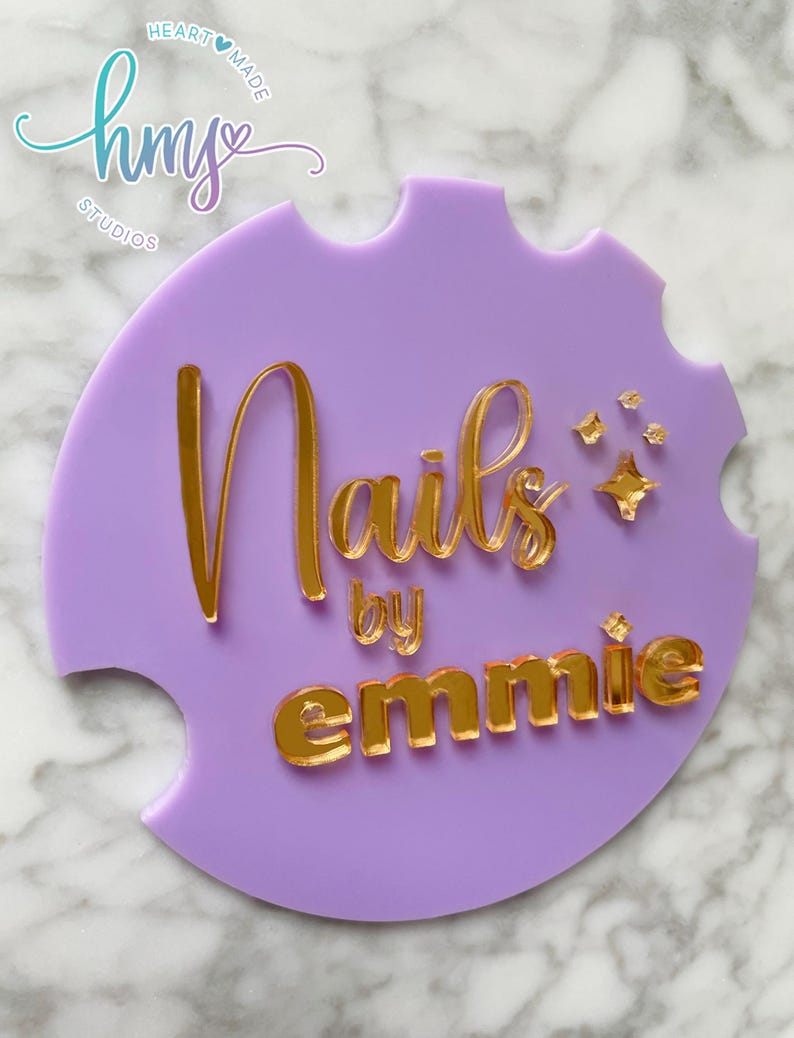 May include: Purple acrylic sign with gold lettering that reads "Nails by emmie" with a small gold star design. The sign has a heart-shaped logo in the top left corner that reads "hmy studios" with a heart.