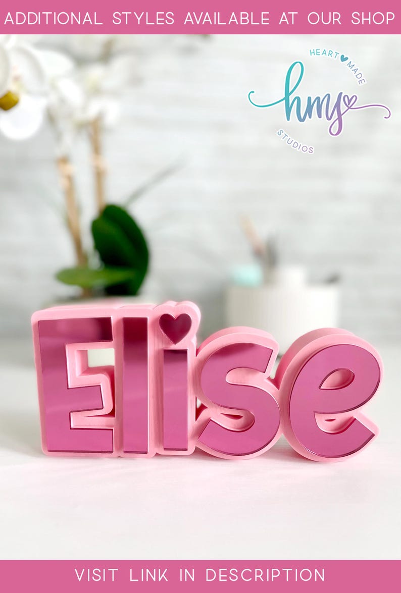 May include: Pink 3D name sign with the name "Elise" spelled out in large letters. The letters are pink with a mirrored finish. A small pink heart is on top of the "E". The sign is on a white surface.  HEART MADE hm STUDIOS VISIT LINK IN DESCRIPTION