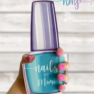 May include: A blue and purple nail polish bottle with the text "nails by Mimi" on the front. The bottle is being held by a hand with pink nail polish.