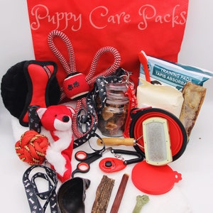 May include: A red tote bag with the words "Puppy Care Packs" printed on it. The bag is filled with various puppy supplies, including a red rope toy, a black and white dog leash, a plush toy, a red chew toy, a dog brush, a bowl, a bag of training pads, and a jar of dog treats.