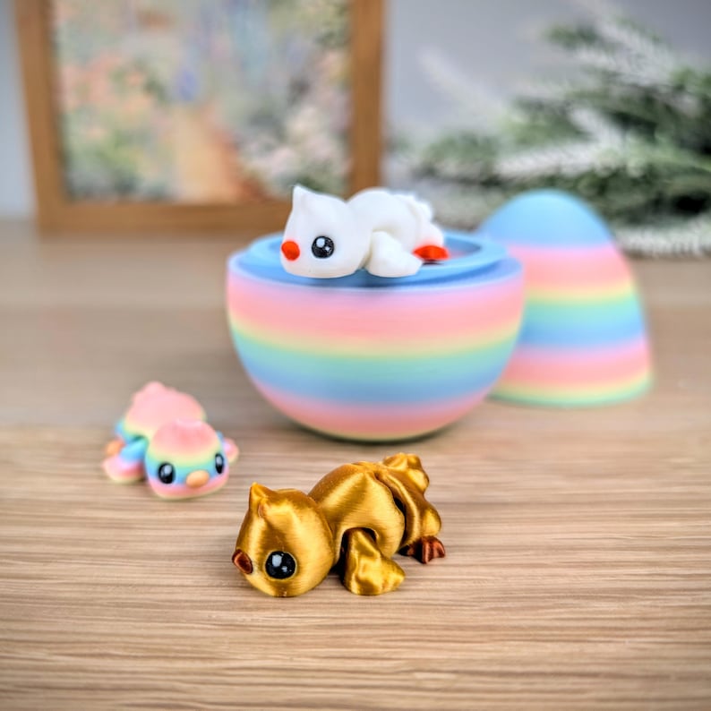 May include: A collection of colorful, whimsical figurines. A gold-colored cat figurine is in the foreground. A rainbow-striped egg-shaped container holds a white seal figurine. A smaller, pastel-colored seal figurine is also present.