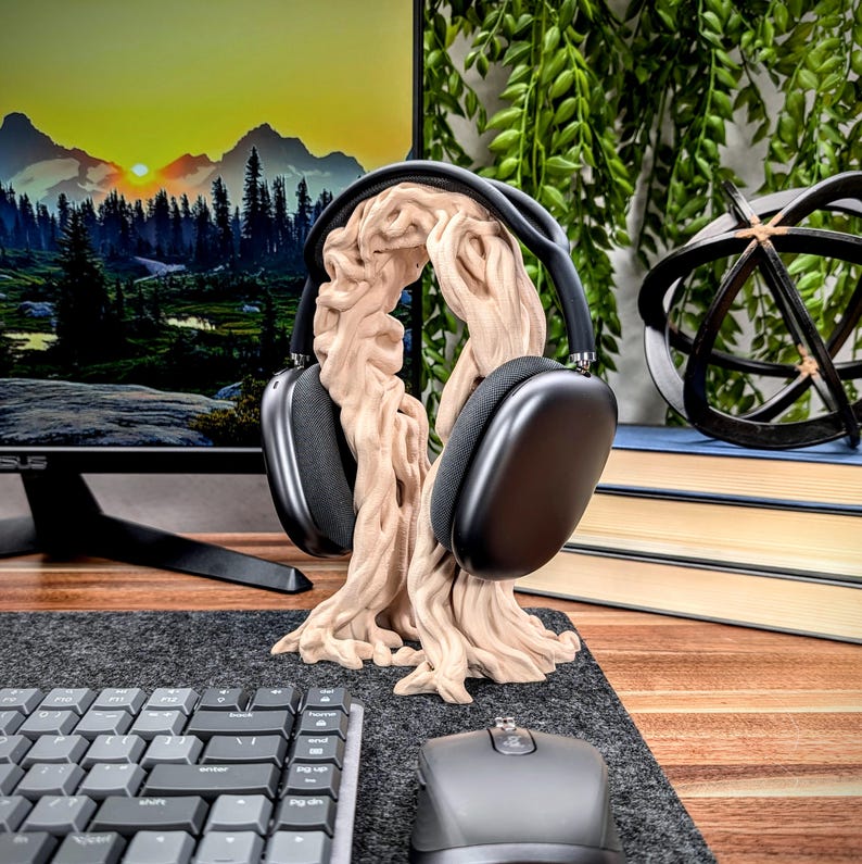 May include: A wooden headphone stand shaped like a tree with a pair of black headphones resting on the branches. The stand is on a desk with a keyboard and mouse.