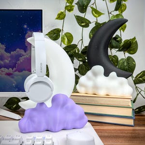 Pode incluir: Esculturas de lua crescente branca e preta com base de nuvem, uma escultura de nuvem roxa e fones de ouvido brancos com a palavra "SONY" no lado.