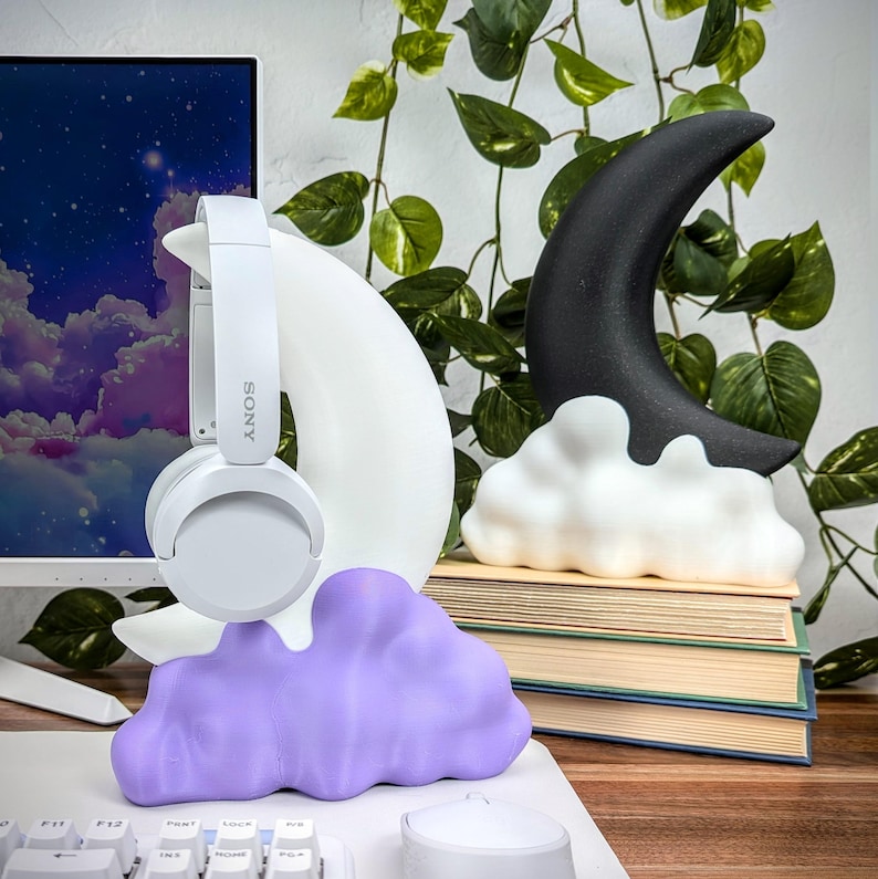 Pode incluir: Esculturas de lua crescente branca e preta com base de nuvem, uma escultura de nuvem roxa e fones de ouvido brancos com a palavra "SONY" no lado.
