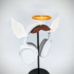Op de afbeelding: Witte gaming headset met een halo en engelenvleugels, gemonteerd op een houten standaard.