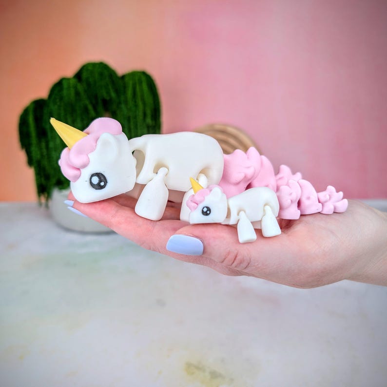 May include: Two white unicorn figurines with pink and yellow accents. The larger unicorn has a long, flowing mane and tail made of pink and white pieces. The smaller unicorn is sitting on the larger unicorn's back.
