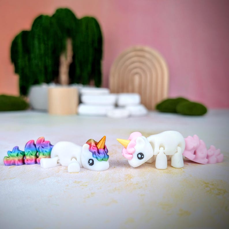 May include: Two small white unicorn figurines with articulated limbs. One unicorn has a rainbow tail and the other has a pink tail.
