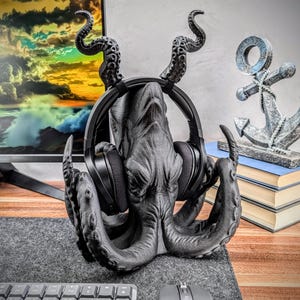 May include: A black octopus-shaped headphone stand with a textured surface. The stand has eight tentacles and is holding a pair of black headphones.
