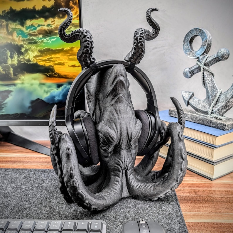 May include: A black octopus-shaped headphone stand with a textured surface. The stand has eight tentacles and is holding a pair of black headphones.