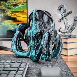 May include: A teal blue 3D printed octopus headphone stand with a textured surface. The octopus has a large head with a pair of headphones in its tentacles.