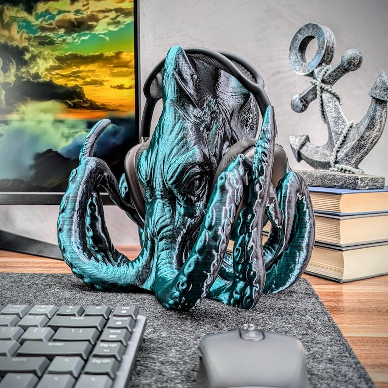 May include: A teal blue 3D printed octopus headphone stand with a textured surface. The octopus has a large head with a pair of headphones in its tentacles.