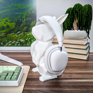 May include: White ceramic headphone stand shaped like a rabbit with a pair of white headphones resting on the stand.