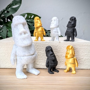 May include: A set of six small statues of Easter Island heads in different colors, including white, gold, and black. The statues are made of a textured material and have a simple, minimalist design.