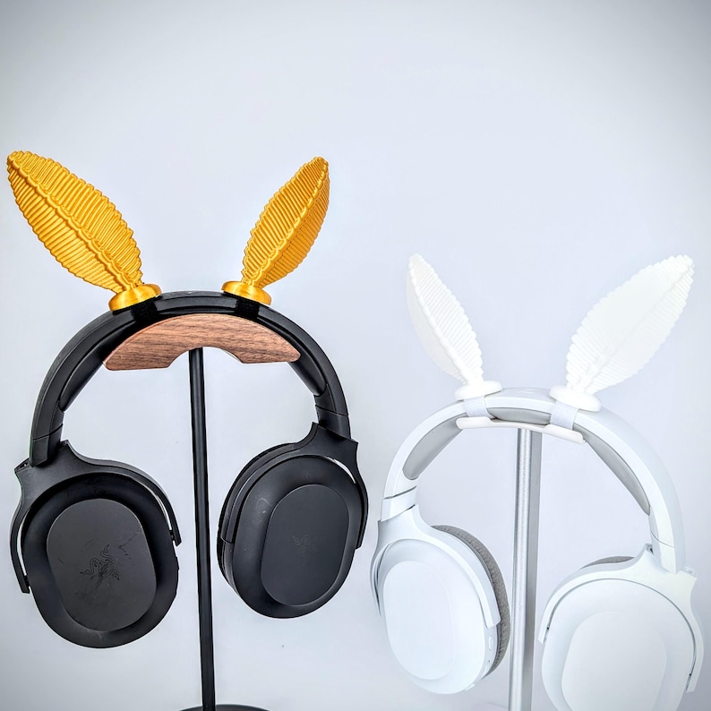 May include: Two headphone stands with black and white headphones. The stands have gold and white bunny ear attachments.
