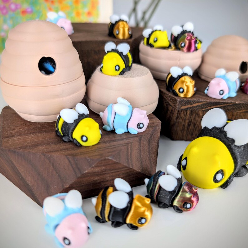 May include: A collection of small, colorful bee figurines, some with black and yellow stripes, others with blue and pink stripes, and some with iridescent wings. The figurines are arranged on a wooden surface, with a larger bee figurine in the foreground.