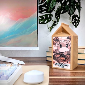 May include: A brown milk carton with a cartoon cow on the front. The carton has the words "Chocolate Milk" printed on it. The carton is sitting on a wooden table.