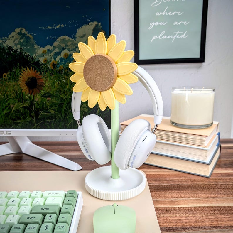 K&ouml;nnte beinhalten: Ein wei&szlig;er Kopfh&ouml;rerst&auml;nder mit Sonnenblumen-Design. Der St&auml;nder hat einen gr&uuml;nen Stiel und eine gelbe Sonnenblume mit brauner Mitte. Der St&auml;nder h&auml;lt ein Paar wei&szlig;e Kopfh&ouml;rer.