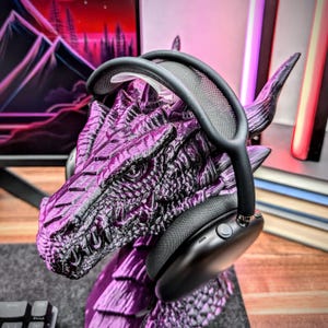 May include: Black over-ear headphones with a mesh headband resting on a purple dragon figurine. The headphones have a button on the side.