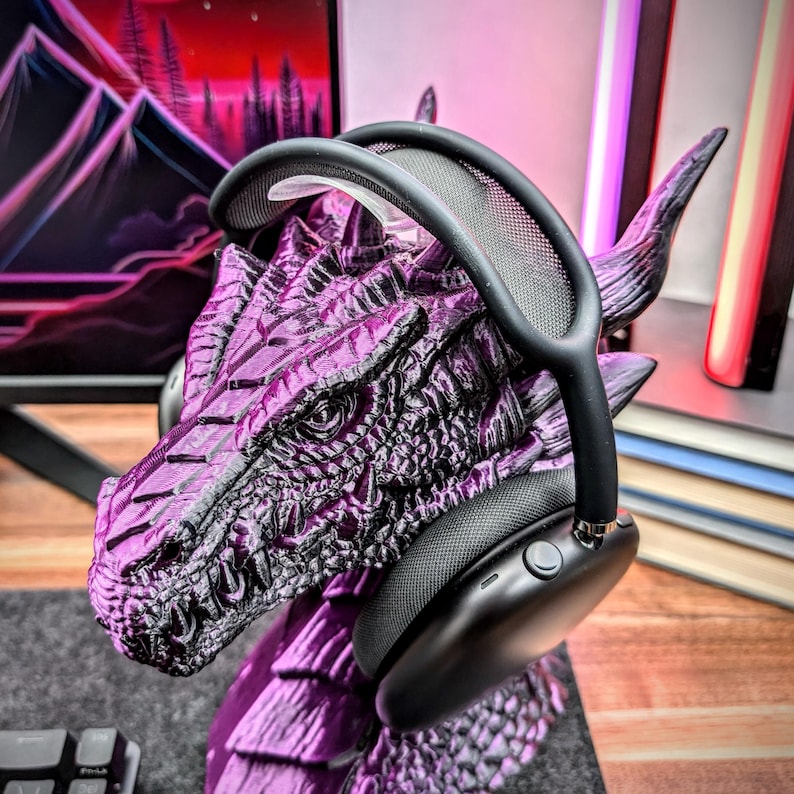 May include: Black over-ear headphones with a mesh headband resting on a purple dragon figurine. The headphones have a button on the side.