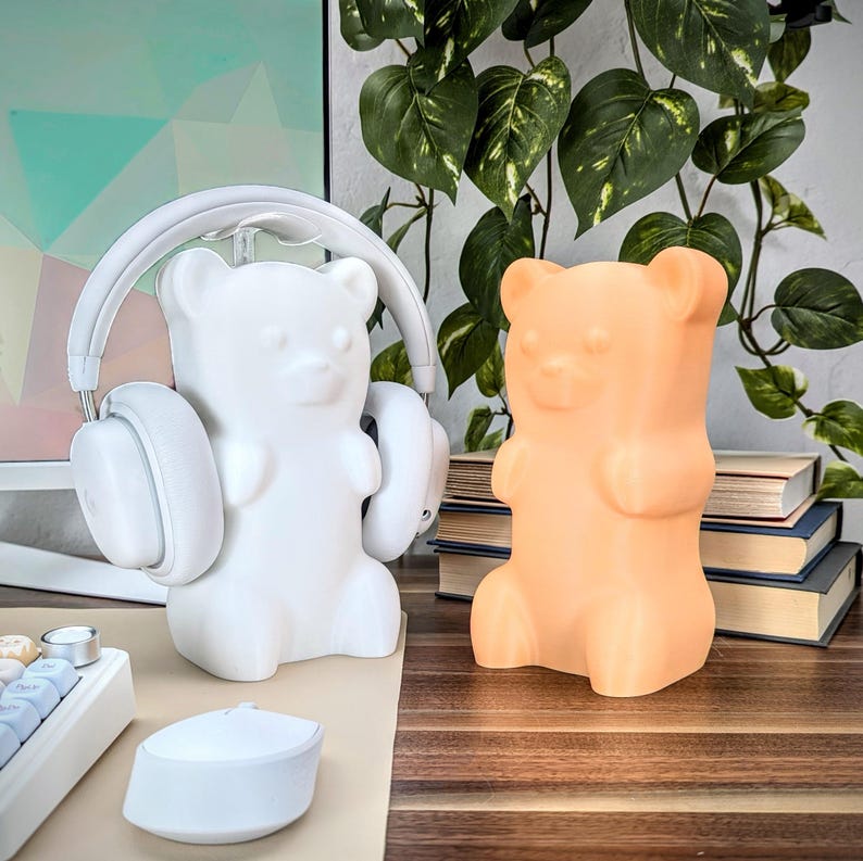 May include: Two gummy bear shaped night lights, one white and one orange, on a wooden surface. The white gummy bear is wearing headphones.