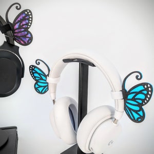 May include: White headphones with a black stand and butterfly decorations. The butterflies are blue and purple.