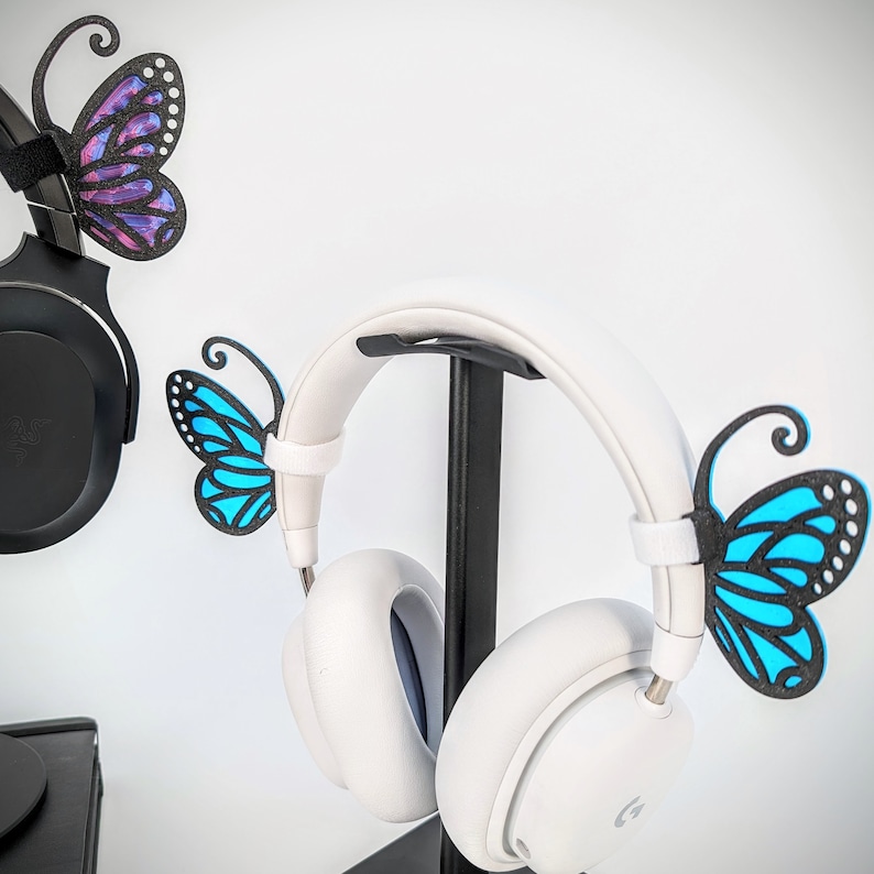 May include: White headphones with a black stand and butterfly decorations. The butterflies are blue and purple.