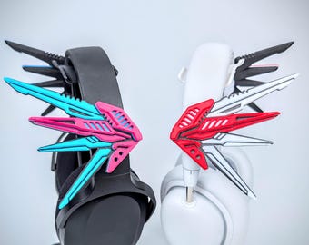 May include: A pair of gaming headsets, one black and one white, each adorned with colorful, angular wing-like attachments. The black headset features blue and pink accents, while the white headset has red and white details. The attachments are designed to enhance the aesthetic of the headsets.