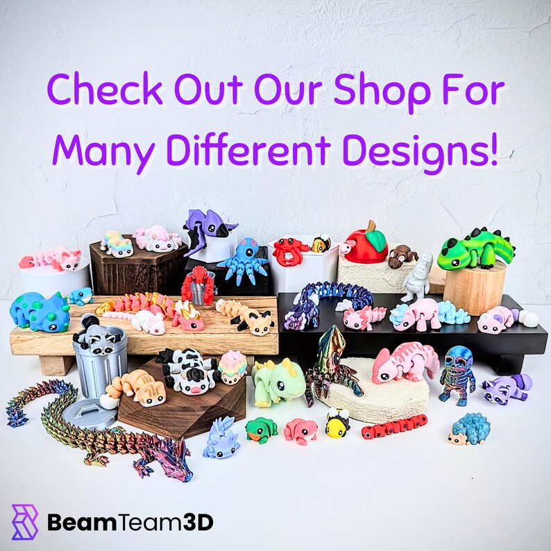 May include: A collection of colorful 3D-printed figurines, including dragons, axolotls, and other creatures, displayed on wooden platforms and white surfaces. The text "Check Out Our Shop For Many Different Designs!" is visible.
