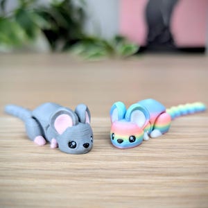 May include: Two small, hand-painted mouse figurines. One is gray with pink ears and the other is rainbow colored with a white belly.