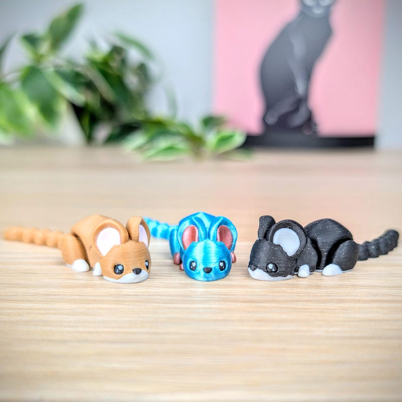 May include: Three small, 3D printed figurines of mice in different colors: brown, blue, and black. The mice are posed in a playful, crouching position.