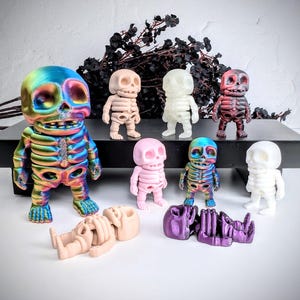 Könnte beinhalten: Eine Sammlung von acht Skelettfiguren in verschiedenen Farben, darunter regenbogenfarben, rosa, weiß und rot. Die Skelette sind in verschiedenen Positionen aufgestellt, einige stehen, einige sitzen und einige liegen. Die Figuren sind aus Kunststoff und haben ein detailliertes Skelettdesign.