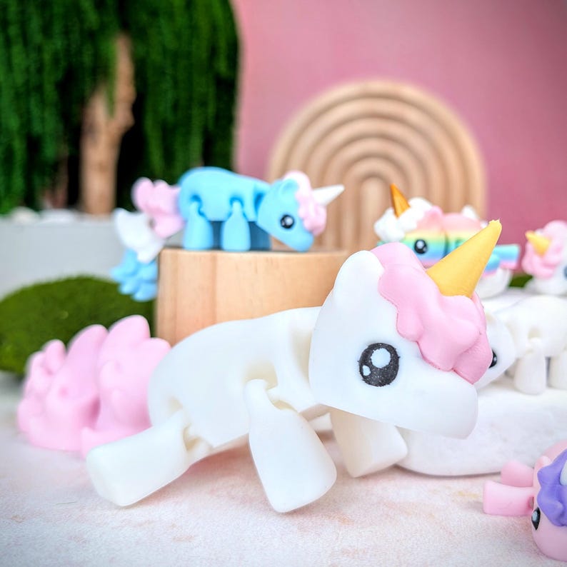 May include: A collection of white, pink, and blue unicorn figurines with articulated limbs. The unicorns have a whimsical, cartoon-like appearance with large eyes and colorful details.