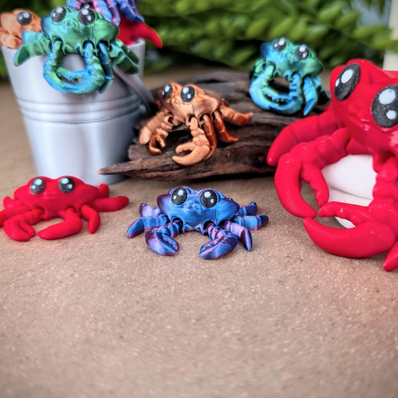 May include: A collection of five small, colorful, 3D printed crabs. The crabs are in various poses and colors, including red, blue, green, and orange.