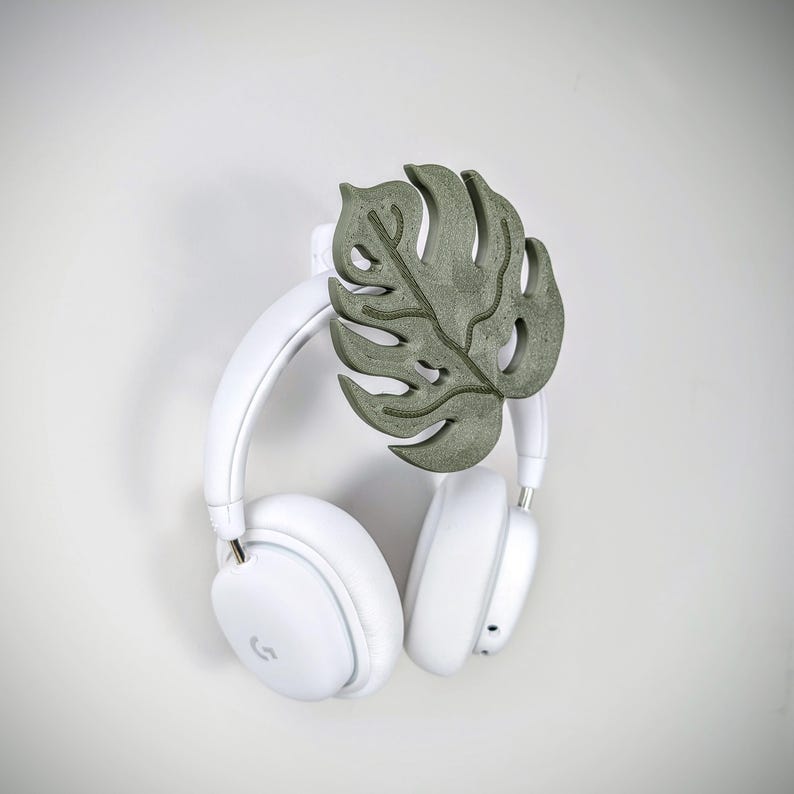 May include: White wireless headphones with a green monstera leaf-shaped headphone stand.