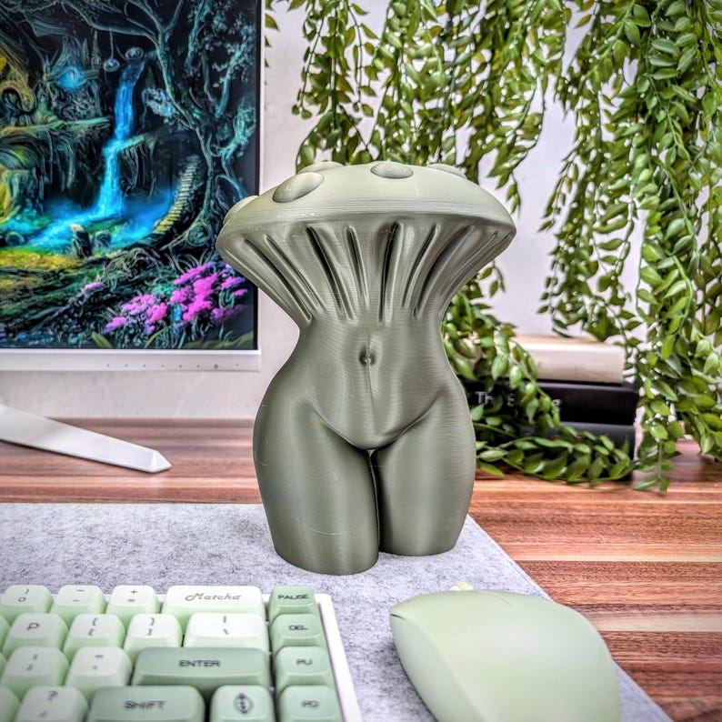 May include: A 3D printed sculpture of a human torso with a mushroom-shaped top. The sculpture is a muted green color and is sitting on a desk.