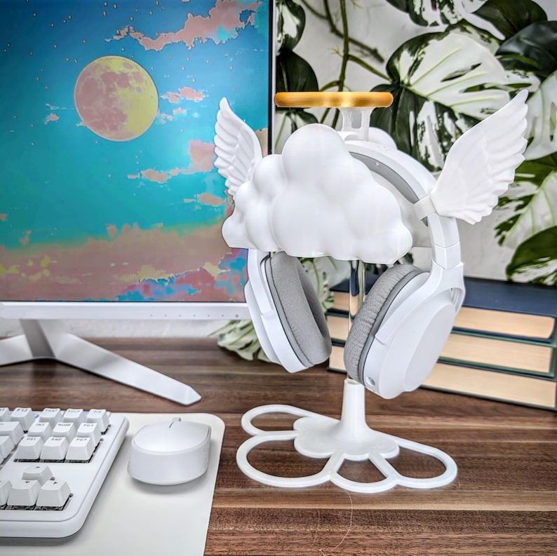 K&ouml;nnte beinhalten: Wei&szlig;er Kopfh&ouml;rerst&auml;nder mit einem Wolken- und Engelsfl&uuml;gel-Design. Der St&auml;nder hat einen goldenen Heiligenschein und eine wei&szlig;e Basis mit einem blumenf&ouml;rmigen Design.
