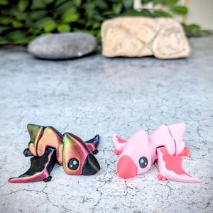 May include: Two small, hand-painted figurines of pterodactyls. One is pink and the other has iridescent wings with a black body.