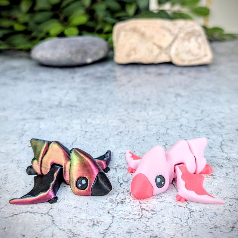 May include: Two small, hand-painted figurines of pterodactyls. One is pink and the other has iridescent wings with a black body.