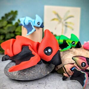 May include: A collection of five small, colorful, 3D printed figurines of mythical creatures. The figurines are made of plastic and have a variety of colors, including red, green, blue, and black. The figurines are posed in a variety of positions, and some have wings.