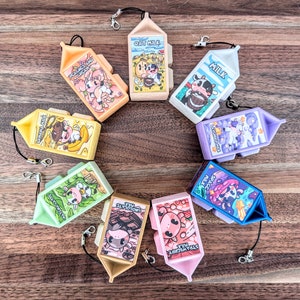 May include: Nine colourful milk carton keychains with different flavours and cartoon animal illustrations. The flavours include: Oat Milk, Milk, Lavender Milk, Banana Milk, Matcha Latte, Space Milk, Chocolate Milk, Strawberry Milk, Peaches and Cream.
