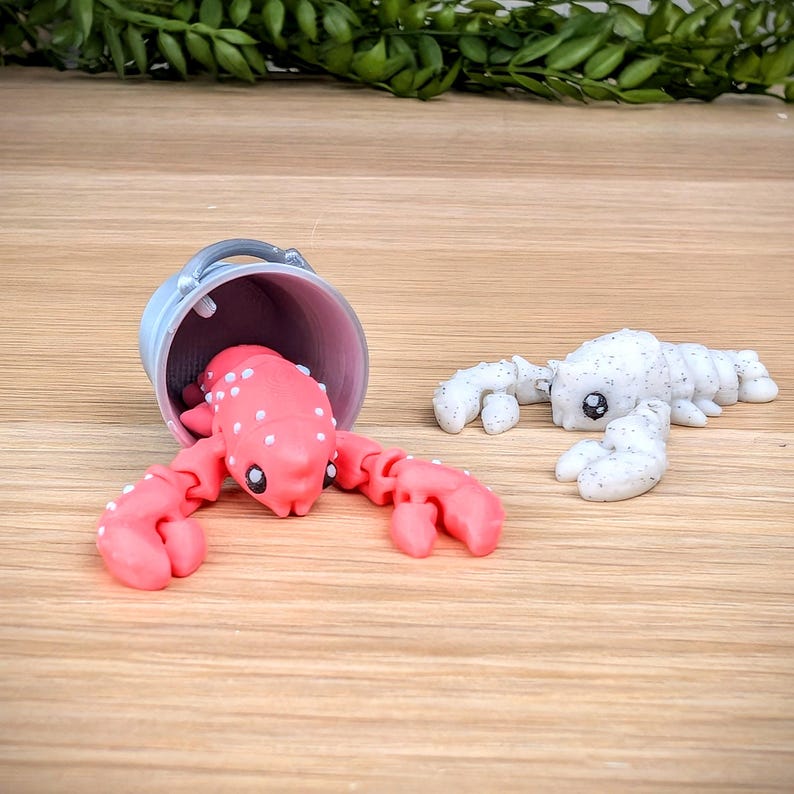 May include: Two small lobster figurines, one pink with white spots and one white with black spots. The pink lobster is in a small grey bucket.