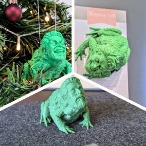 May include: A bright green 3D printed figurine of a toad with a human face. The toad has textured skin and a detailed human head with a beard and hair. The figurine is shown in three different settings, including hanging as an ornament.
