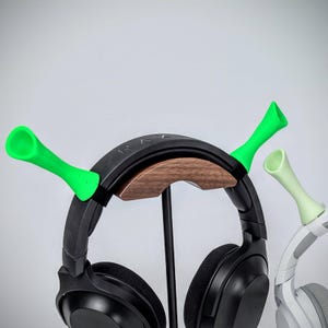 May include: Black headphones with a wooden accent, held by a black stand. Two green and one light green earbud holders are attached to the headphones. The word "RAZER" is visible on the headphones.