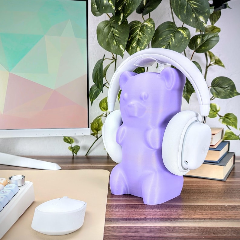 May include: A purple gummy bear shaped headphone stand. The stand is made of plastic and has a white pair of headphones resting on it.