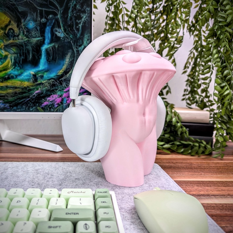 May include: A pink ceramic sculpture shaped like a mushroom with a white pair of headphones on top. The sculpture is on a desk with a green keyboard and a green mouse.