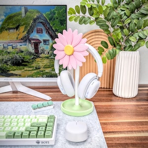 May include: A pink flower-shaped headphone stand with a pair of white headphones hanging on it. The stand is on a wooden desk with a keyboard and a mouse.