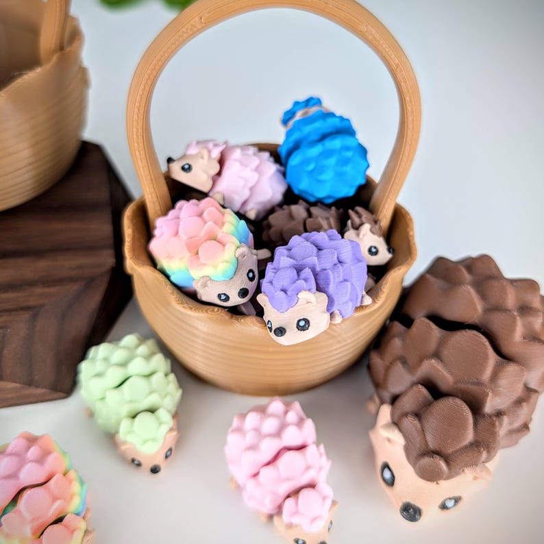 May include: A brown wicker basket filled with colourful hedgehog figurines. The hedgehogs are in various colours, including pink, blue, purple, and rainbow. There are also two brown hedgehog figurines outside of the basket.