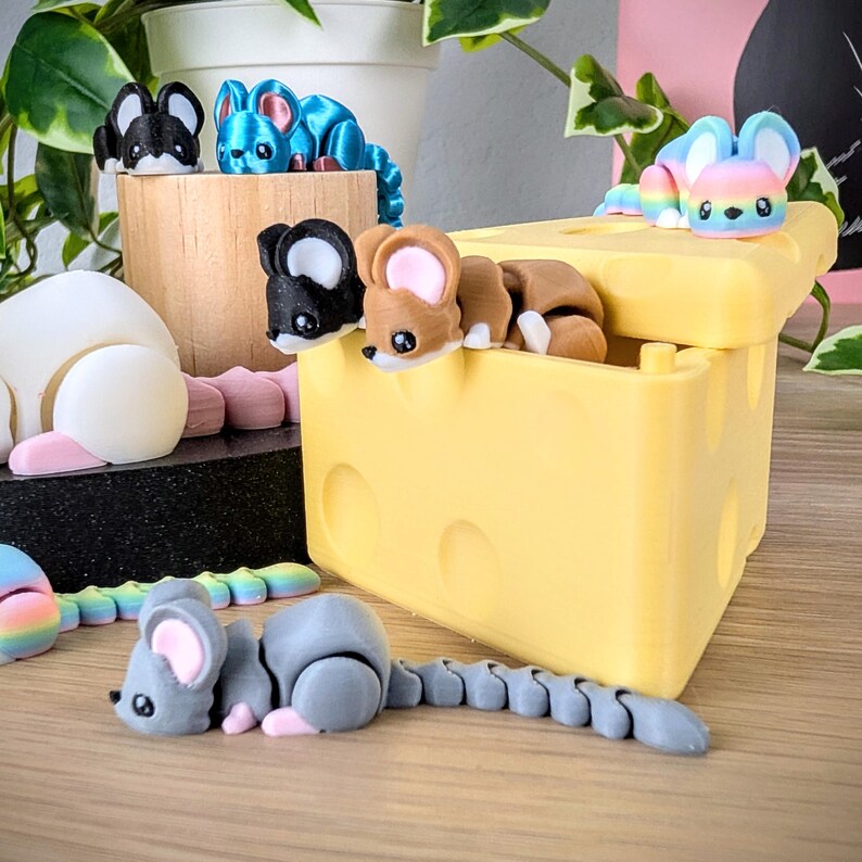 May include: A yellow cheese-shaped box with a removable lid. The box is open and contains several small, colorful mouse figurines. The box is sitting on a wooden surface.