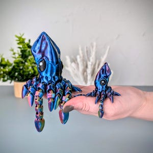 May include: Two iridescent blue and purple 3D printed squid figurines. The larger squid is about 5 inches tall and the smaller squid is about 2 inches tall.